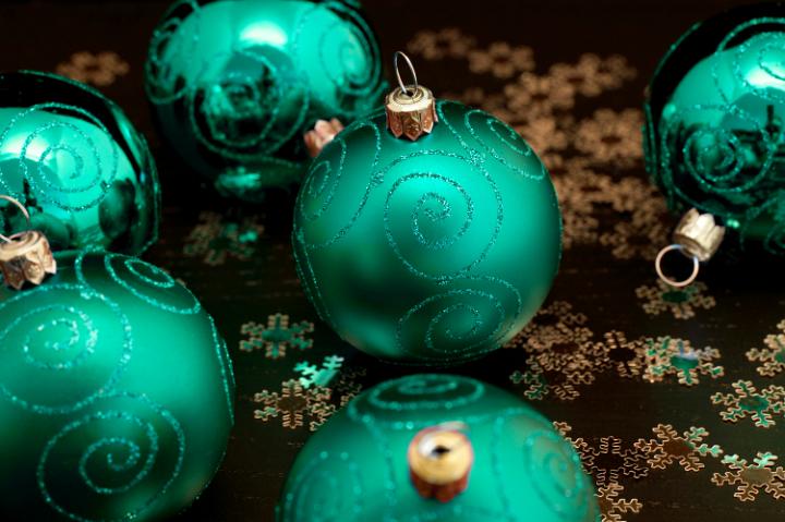 Emerald green Christmas balls patterned with glitter curlicues amongst scattered golden snowflakes