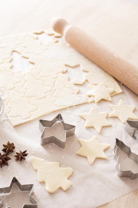 Baking delicious homemade spicy Christmas biscuits with rolled pastry shapes cut with star and tree shaped cookie cutters on a wooden kitchen counter