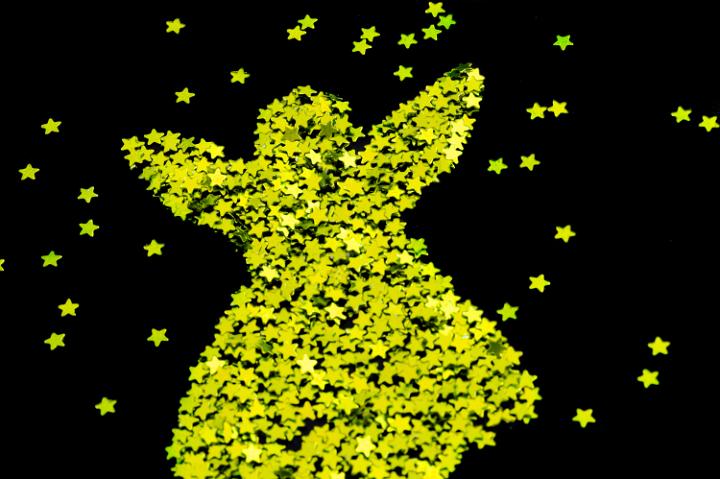 Gold stars arranged in the shape of a joyful Christmas angel surrounded by randomly scattered stars on a black background