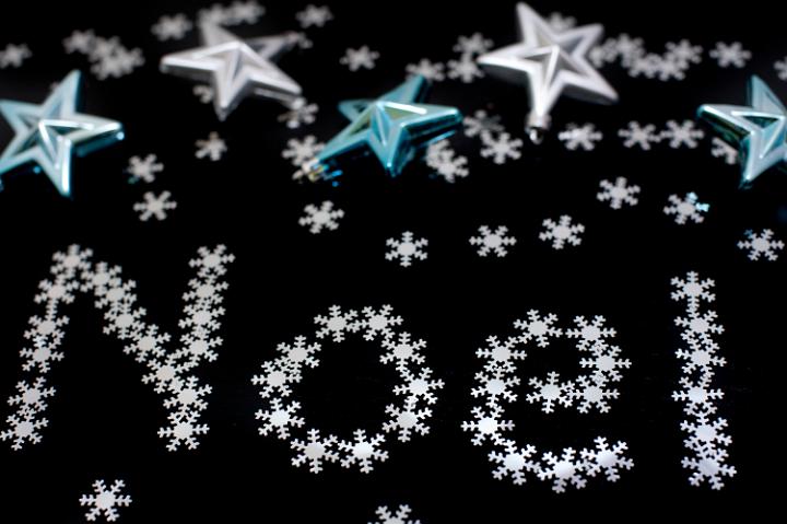 Noel greetings message with letters formed of tiny snowflakes on a dark background with Christmas stars