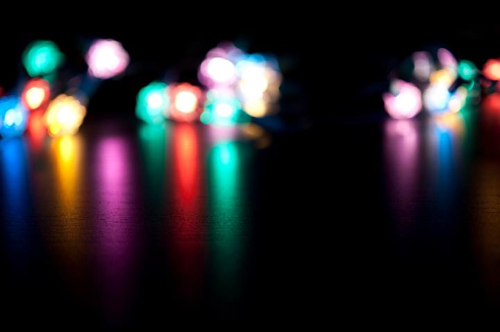 Blurred colourful festive lights in the distance casting long reflections across the surface towards the camera on a black background with copyspace