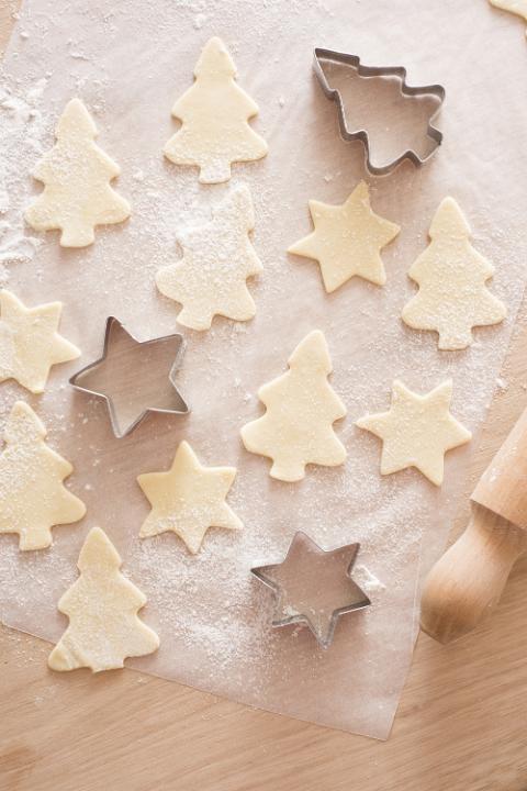 Christmas baking of traditional festive cookies in tree and star shapes with an overhead view of metal cookie cutters and cut out raw pastry on floured paper on a kitchen counter
