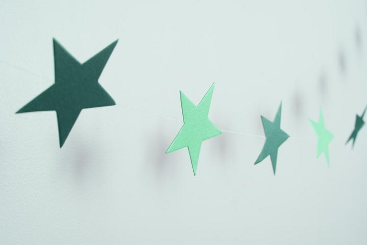 String of simple green Christmas paper stars hanging on a white wall in an oblique view with copy space