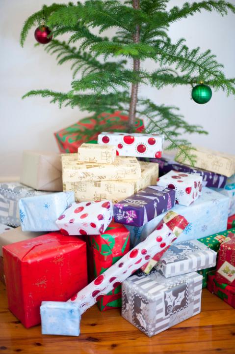 Christmas presents in colourful giftwrap piled at the foot of the Christmas tree ready for a family gathering to celebrate the festive season