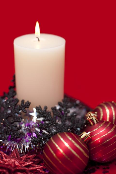 an arrangement of a christmas candle and various festive decoration including baubles and tinsel