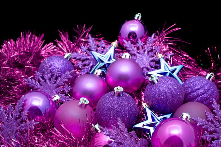 Background arrangement of purple Christmas decorations with tinsel, stars, baubles and snowflakes