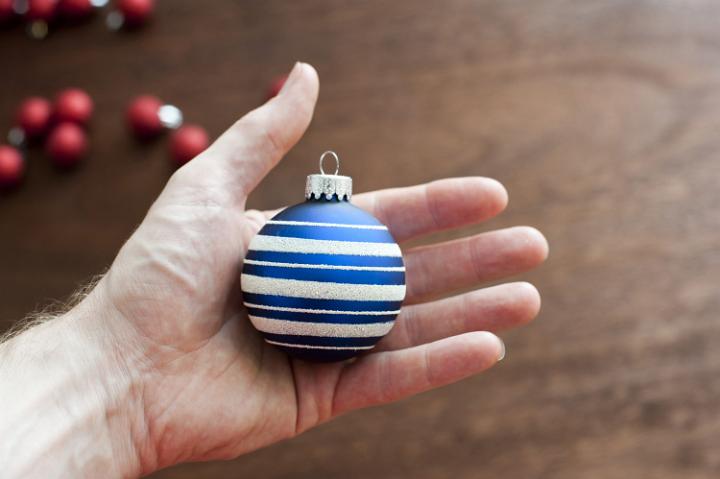 holding blue Christmas ball with a scattering of red christmas baubles in the background