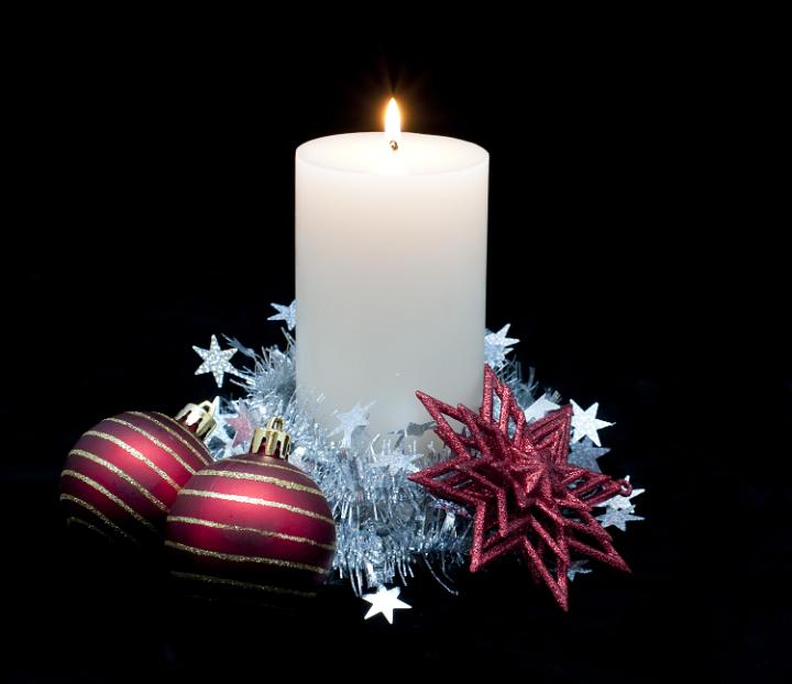 a large pillar candle surrounded by seasonal decorations on a black backdrop