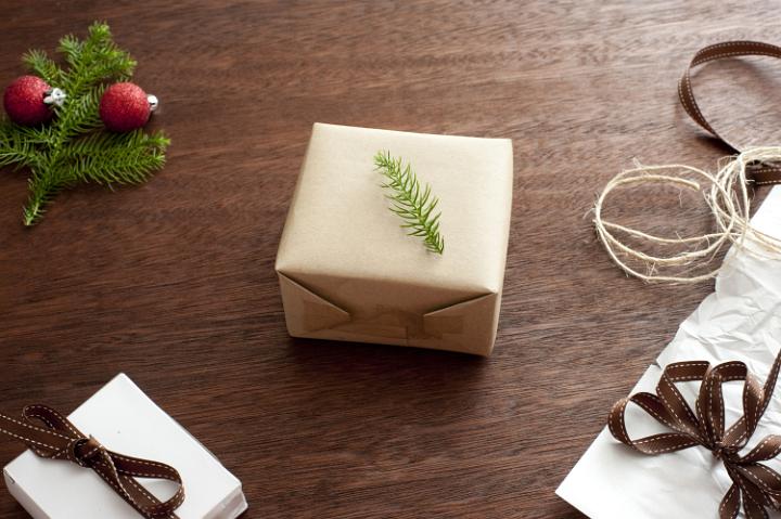 Wrapped present with fir tree branch above. Ribbons and Christmas decoration on wooden table. From above