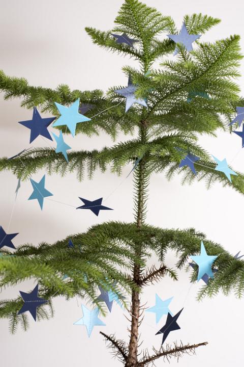 Sparsely decorated natural pine Christmas tree hung with blue paper stars for a simple rustic celebration