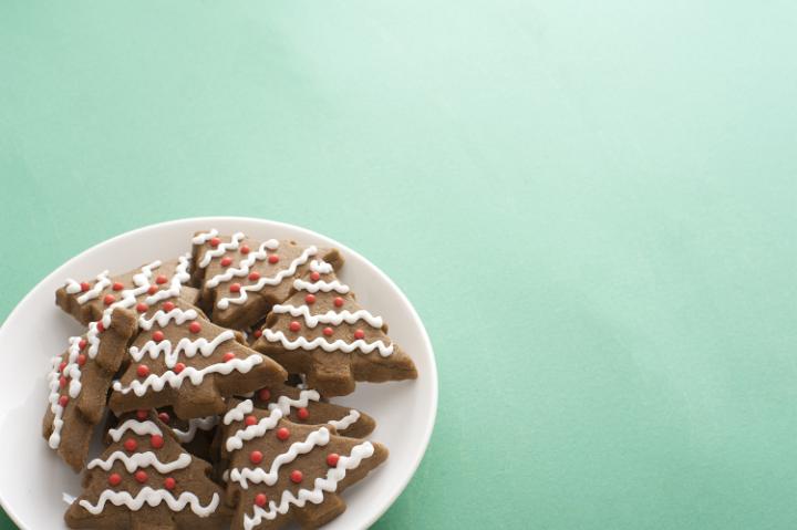Plate of crunchy decorated tree shaped Christmas gingerbread cookies on a green background with copy space for your greeting