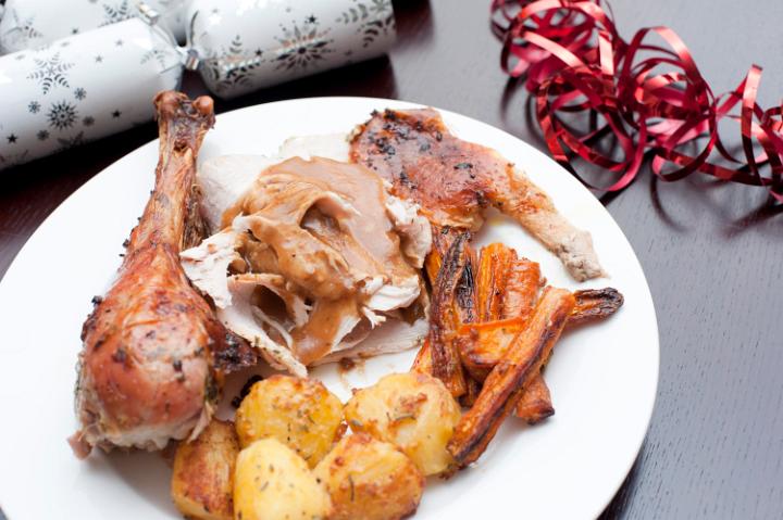 Serving of festive roast turkey topped with gravy with roasted potatoes and carrots for celebrating a Christmas dinner on a table with Christmas crackers