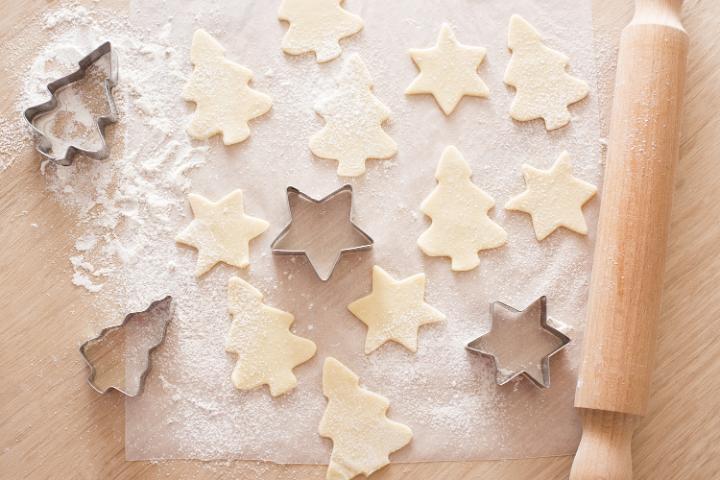 Baking cookies in a christmas kitchen with an overhead view of cookie cutters and cut out shapes in uncooked fresh pastry on floured paper with a rolling pin
