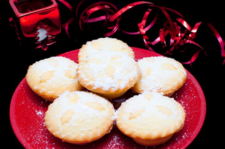Plateful of traditional fruity Christmas mince pies with freshly baked golden crumbly crusts sprinkled with sugar and decorated with holly leaves on the pastry