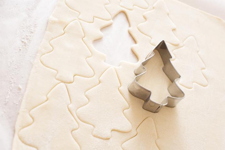 Baking traditional homemade Christmas cookies with rolled fresh dough and a tree shaped cookie cutter in a close up view