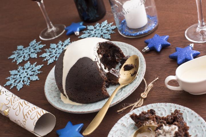 Delicious fruity Christmas pudding with brandy cream being served for dinner on a decorated table with blue snowflakes and stars