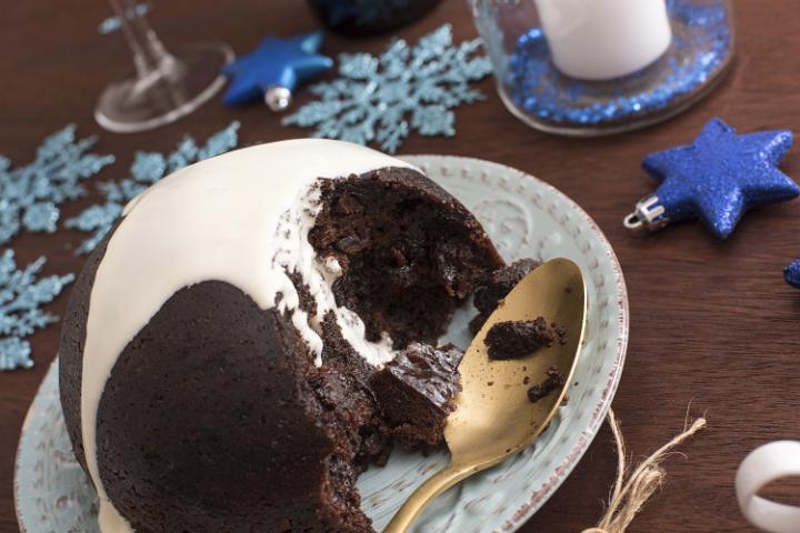 Delicious Christmas fruit pudding topped with brandy cream served on a festive blue themed table in a close up high angle view
