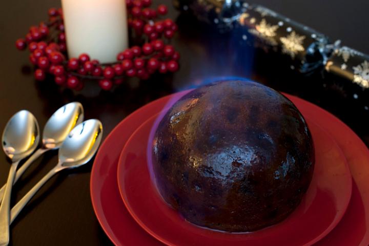 Flaming Christmas pudding set alight with brandy served on a festive seasonal table with decorations as dessert on Christmas day