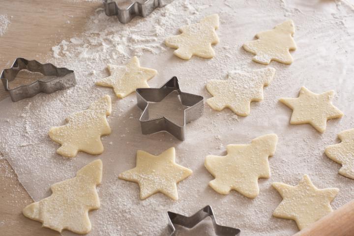 Baking festive tree and star christmas cookies with metal cookie cutters and uncooked pastry shapes on oven paper in a seasonal kitchen