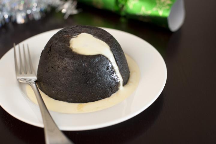 a large christmas plumb pudding on a plate drizzled with brandy custard