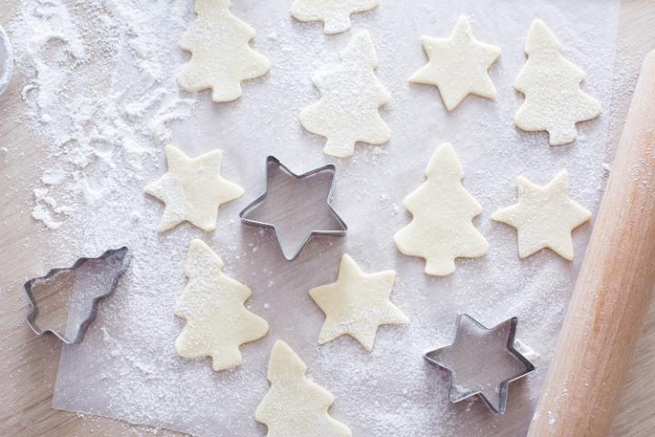From above view of cookies and cutters lying on parchment paper with rolling pin aside.
