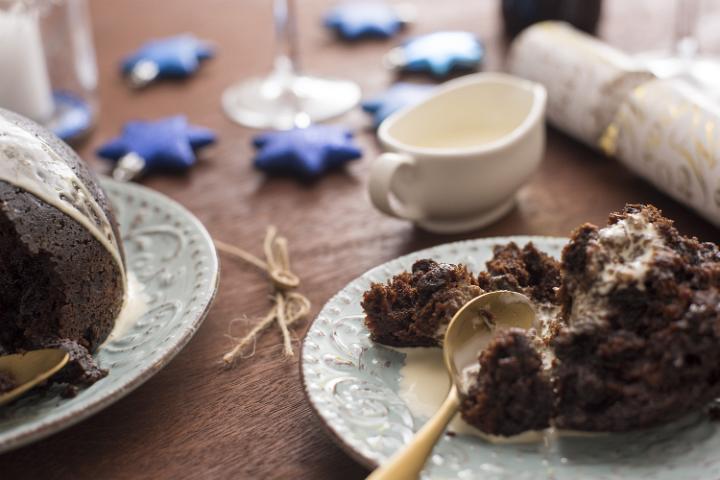 Eating a plate of delicious traditional boiled fruity homemade Christmas pudding served with brandy sauce on a festive table, low angle close up view of the serving