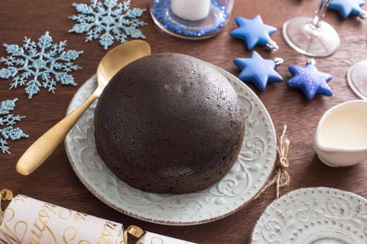Delicious whole uncut Christmas fruit pudding served on a festive Xmas table with decorations and a sauce boat of brandy cream, high angle view