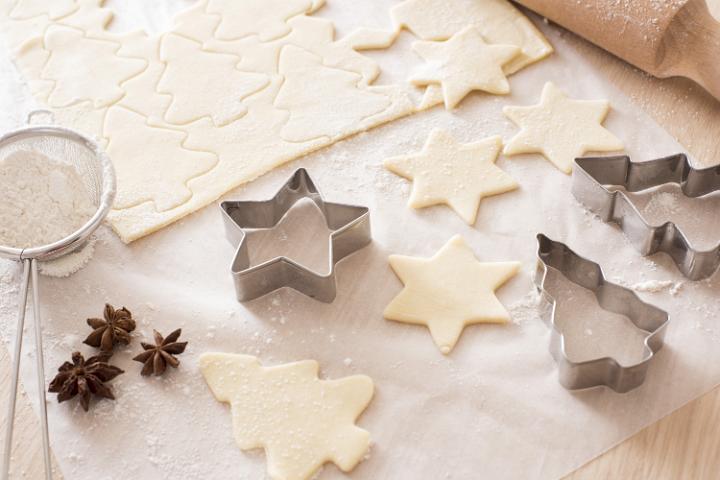 Baking traditional spicy Christmas cookies with star anise and cut out uncooked pastry tree and star shapes alongside seasonal metal cutters on oven paper on a wooden kitchen counter