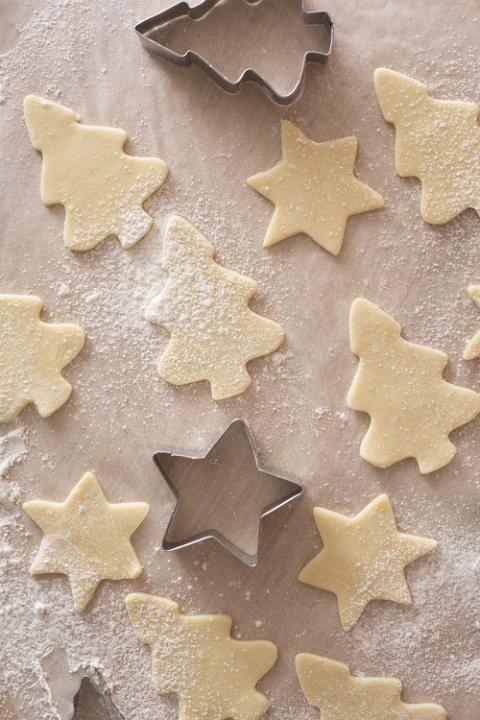 Baking homemade Christmas cookies with an overhead view of uncooked star and tree shaped pastry and cookie cutters on floured oven paper