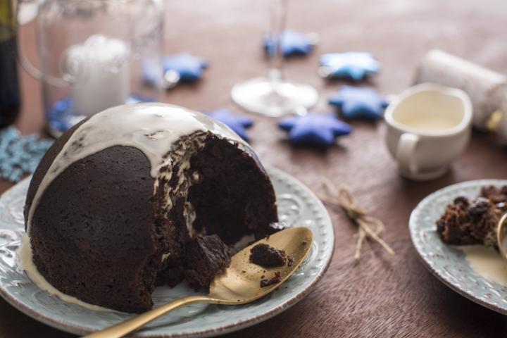 Serving Christmas pudding topped with brandy sauce for dessert at a festive Xmas table with candles and stars