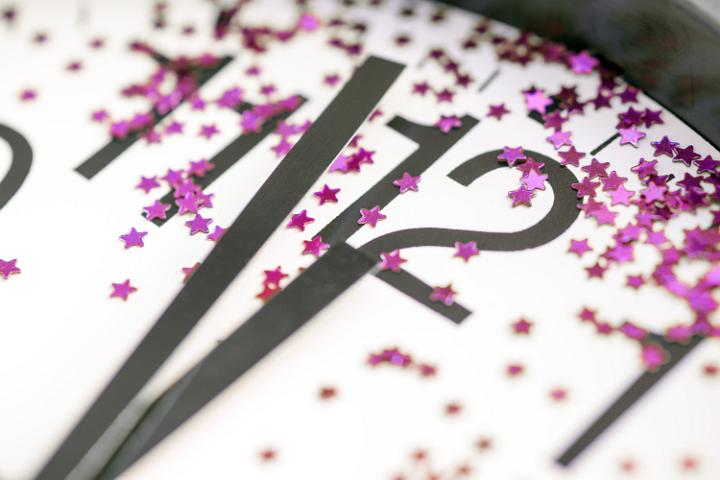 Clock decorated with colorful pink scattered stars striking midnight on New Years Eve in a close up view of the dial and hands