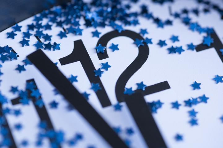 Blue stars on a clock dial counting down to midnight for a New Years Eve celebration in a close up view on the twelve and hands