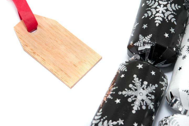 Decorative black Christmas cracker with a pretty snowflake pattern with a blank wood textured gift tag on a white background