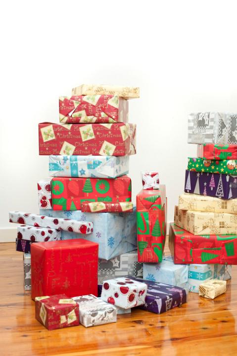 Stacks of multicoloured Christmas gifts wrapped in a variety of colourful paper with seasonal patterns standing on a hardwood floor in the house