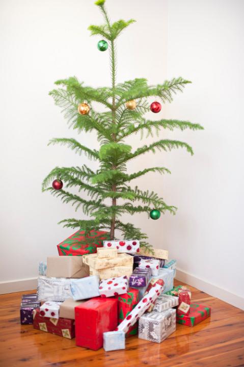 Modern simple natural Christmas tree decorated with colourful baubles and surrounded by a heap of gift-wrapped presents for a family celebration