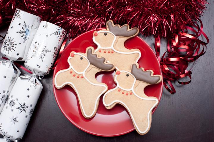 Decorative reindeer Christmas cookies on a plate with chocolate antlers and red noses on a festive table with crackers and tinsel, high angle view