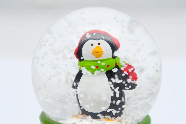 Cute little penguin in his winter cap and scarf standing in a swirling snowstorm in a spherical Christmas snow globe