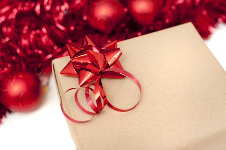 Brown paper wrapped Christmas gift with a festive metallic red ribbon bow and a background of tinsel and ornaments, copy space for your greeting