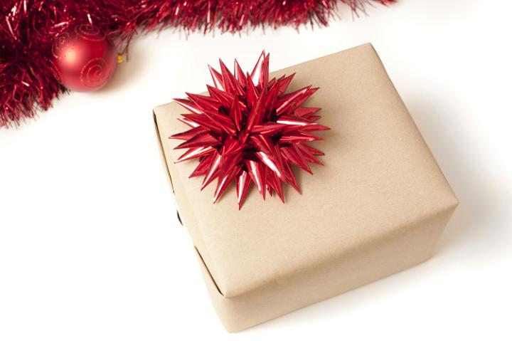 Plain brown paper wrapped gift with Xmas bow and border of tinsel and Christmas baubles on white with copy space