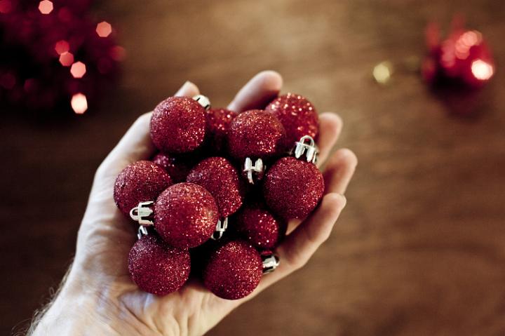 Man's hand holding pile of red sparkling Christmas tree balls