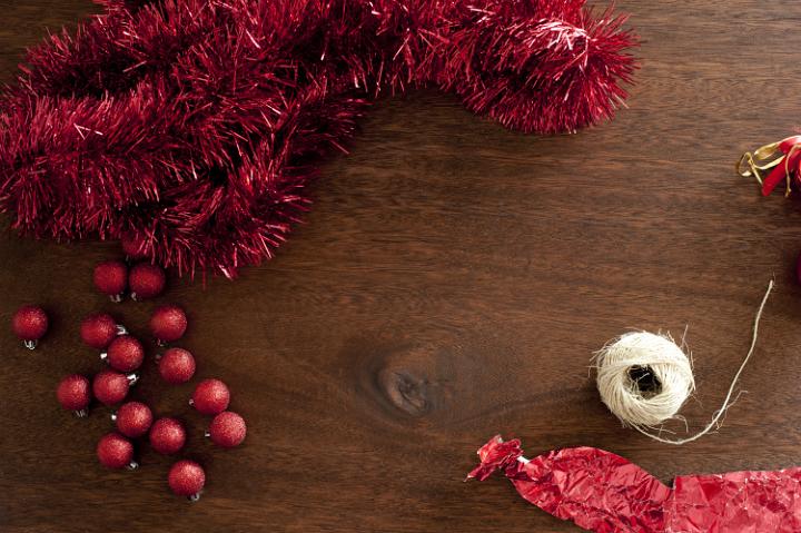 Red Christmas decorative elements: rope, glare, wrapping and balls on wooden table. From above