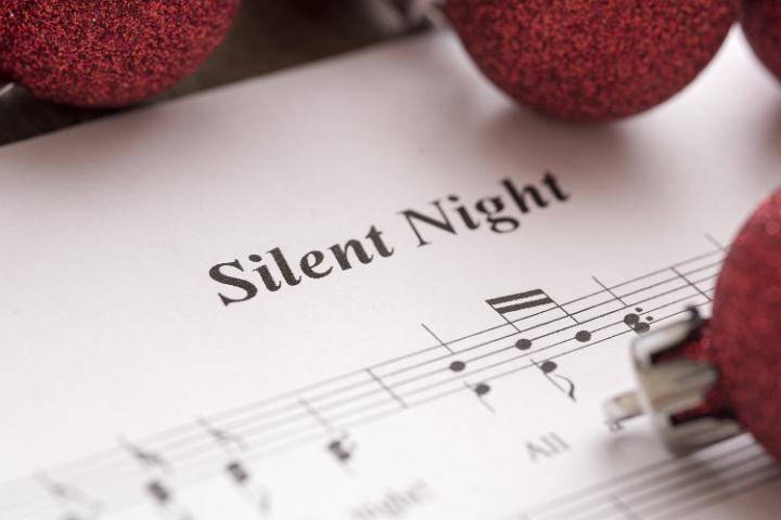 Silent Night music score background with festive red Christmas baubles in a close up view