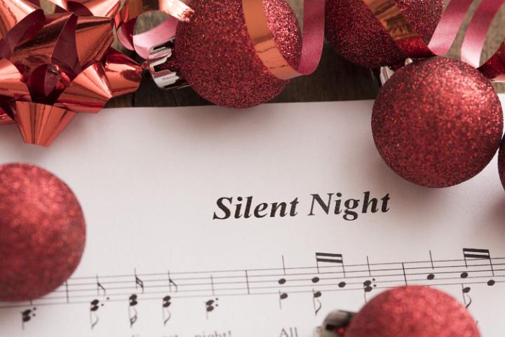 Festive red Christmas carol background with assorted baubles and bows forming a frame around the music score for Silent Night