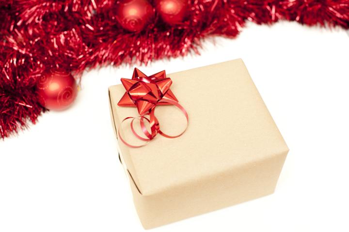Elegant plain wrapped Christmas gift with bow isolated on white with copy space and a top border of red tinsel and baubles, high angle view
