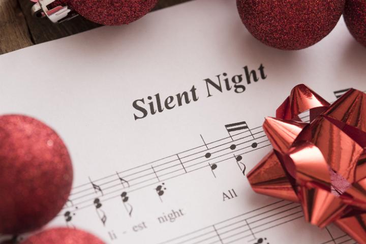 Festive Christmas carol background with the music score for Silent Night decorated with red Xmas decorations in a close up view