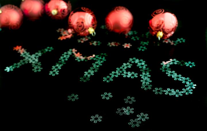 Xmas greeting card with the word Xmas written in small ornamental snowflakes with red Christmas baubles behind