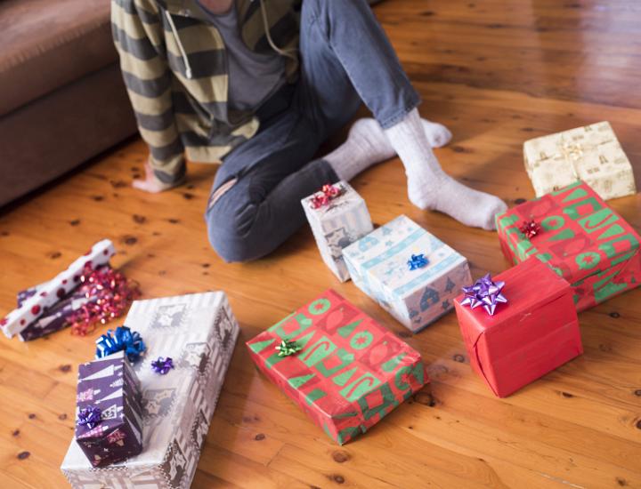 A person sitting on the floor at home in front of a bunch of Christmas gifts wrapped in colorful boxes