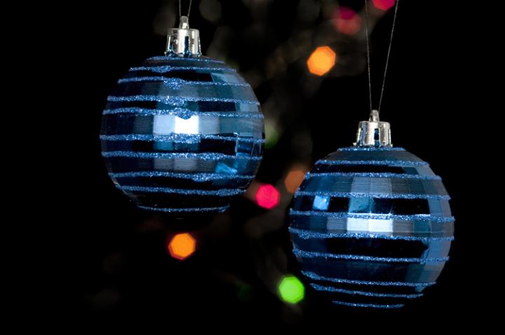 two christmas tree balls hanging on a dark backdrop of frestive colourful lights in the rear