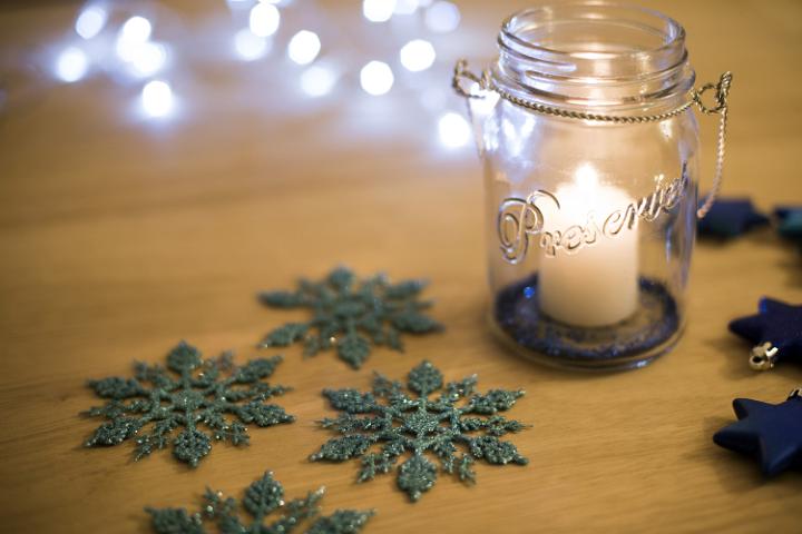 Christmas snowflake and star table decorations and glowing candle in a glass jar with a background bokeh of sparkling white lights